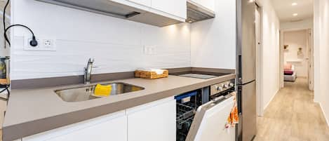 Una cocina moderna con lavavajillas integrado, electrodomésticos de acero inoxidable y encimera gris.