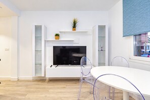 A modern living room with a flat-screen TV mounted on the wall, a dining table with transparent chairs, and a potted plant on a shelf. - Cubo's Apartment Front Line Beach Fuengirola / First line of beach / Air conditioning (Fuengirola)