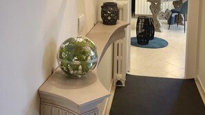 Un couloir agrémenté d’un luminaire décoratif fixé au mur, d’un bol en verre transparent contenant des plantes et d’une petite table sur laquelle se trouve un objet noir.