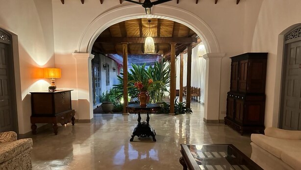 A spacious lobby with a polished floor, a ceiling fan, a chandelier, and a large plant in the center.