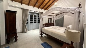 A bedroom with a canopy bed, a wooden wardrobe, a blue rug, and a ceiling fan.