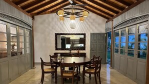 A dining area with a round table and six chairs, a large mirror above the table, and a ceiling fan.