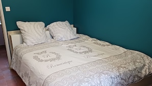A bed with a patterned bedspread and pillows, a white nightstand, and a teal wall.