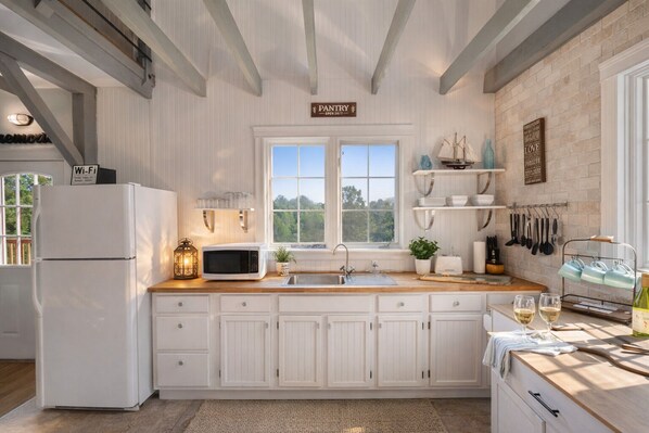A kitchen with white cabinetry, a white refrigerator, a microwave, a sink, and a window with a view of greenery.