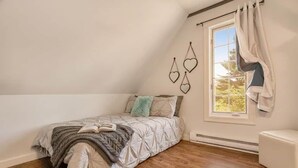 Ein Schlafzimmer mit einem Bett, einem Fenster mit Vorhängen und Blick auf Bäume.