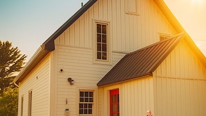 A two-story white wooden house with a red door, surrounded by a garden with various flowers. - Tranquil Coastal 2-Acre Retreat • Near Lunenburg (Mahone Bay)