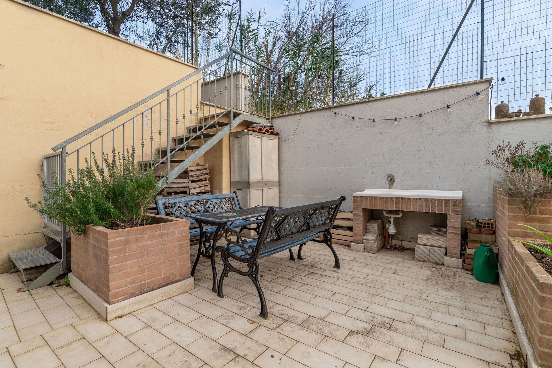 Un patio con tavolo e panche, un caminetto in mattoni e una scala che conduce a un livello superiore.