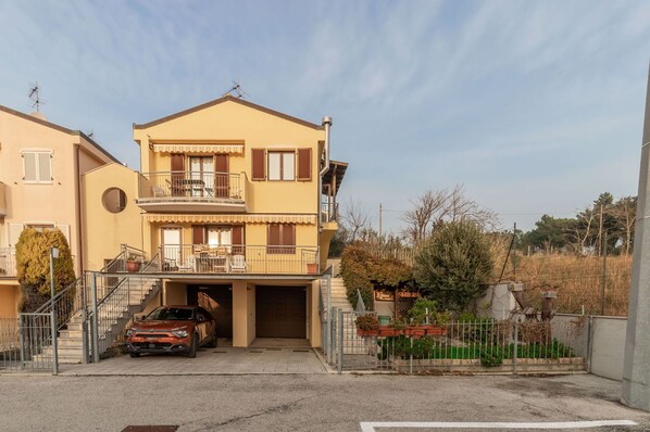 A two-story residential building with a garage entrance, a car parked in front, and a fenced garden area. - Italian Experience- Casale Al Mare (Montorso)