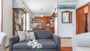 A living room with a grey sofa, a small table with a book and an orchid, and a kitchen in the background. - Italian Experience- Casale Al Mare (Montorso)