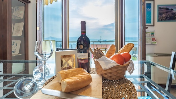 A table with a bottle of wine, a glass, bread, and a basket of oranges by a window with a view of the sea. - Italian Experience- Casale Al Mare (Montorso)