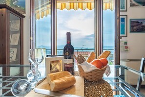 A table with a bottle of wine, a glass, bread, and a basket of oranges by a window with a view of the sea. - Italian Experience- Casale Al Mare (Montorso)