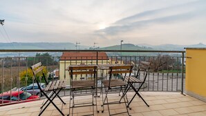 A balcony with a view of a hilly landscape, a yellow building, and a red car parked nearby. - Italian Experience- Casale Al Mare (Montorso)