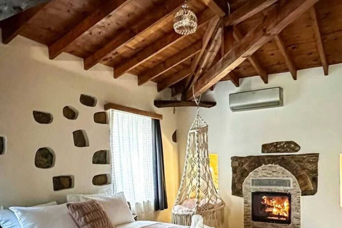 Quarto com lareira de pedra, cama com manta rosa e luminária pendente.