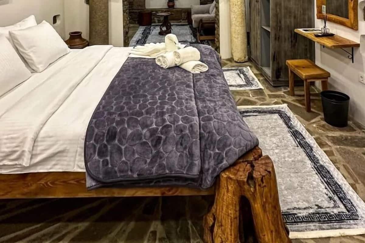 Quarto com arco de pedra, cama com cabeceira de madeira e piso de madeira rústico.