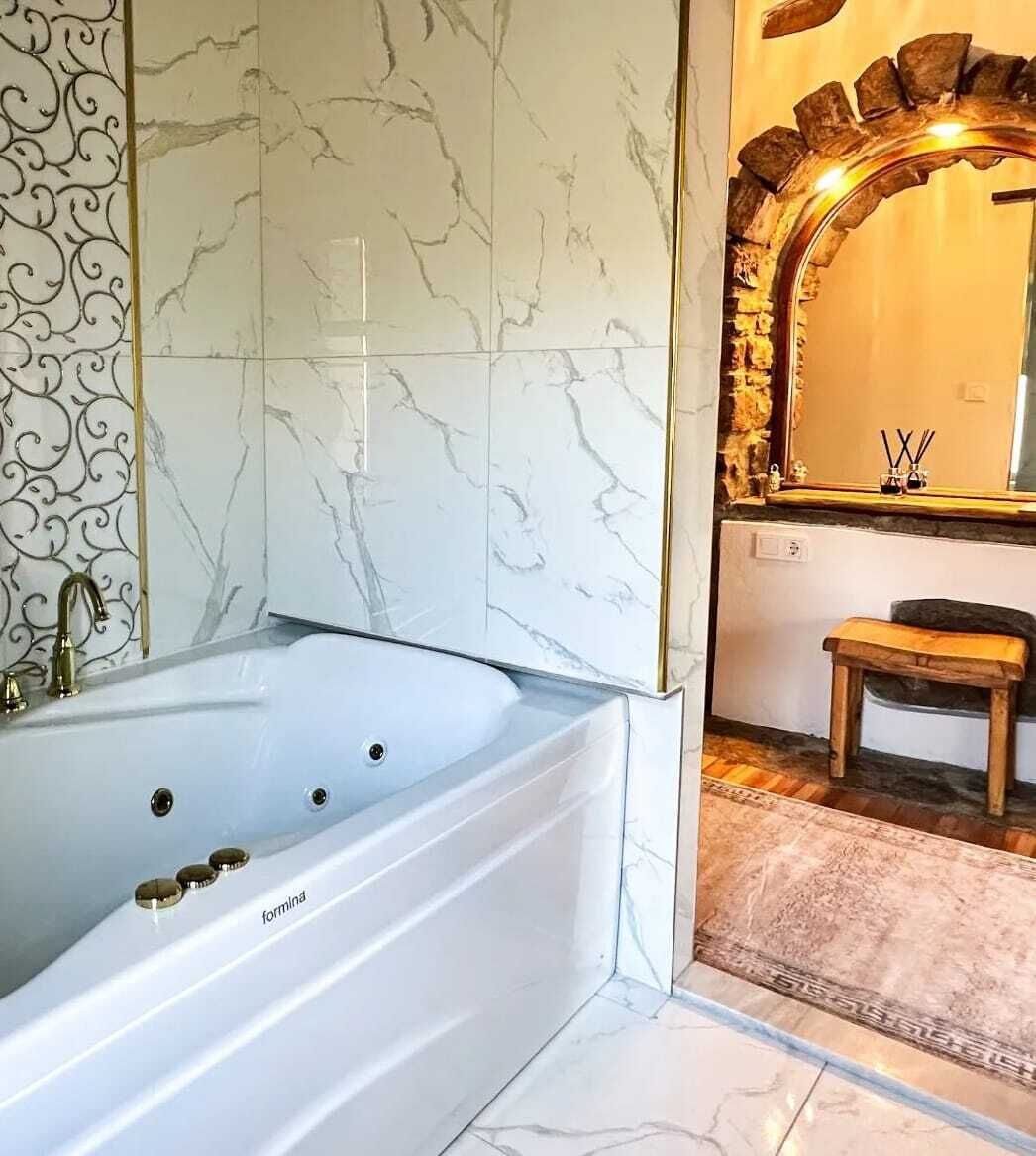 Un baño moderno con una bañera independiente, paredes de mármol y un espejo decorativo.