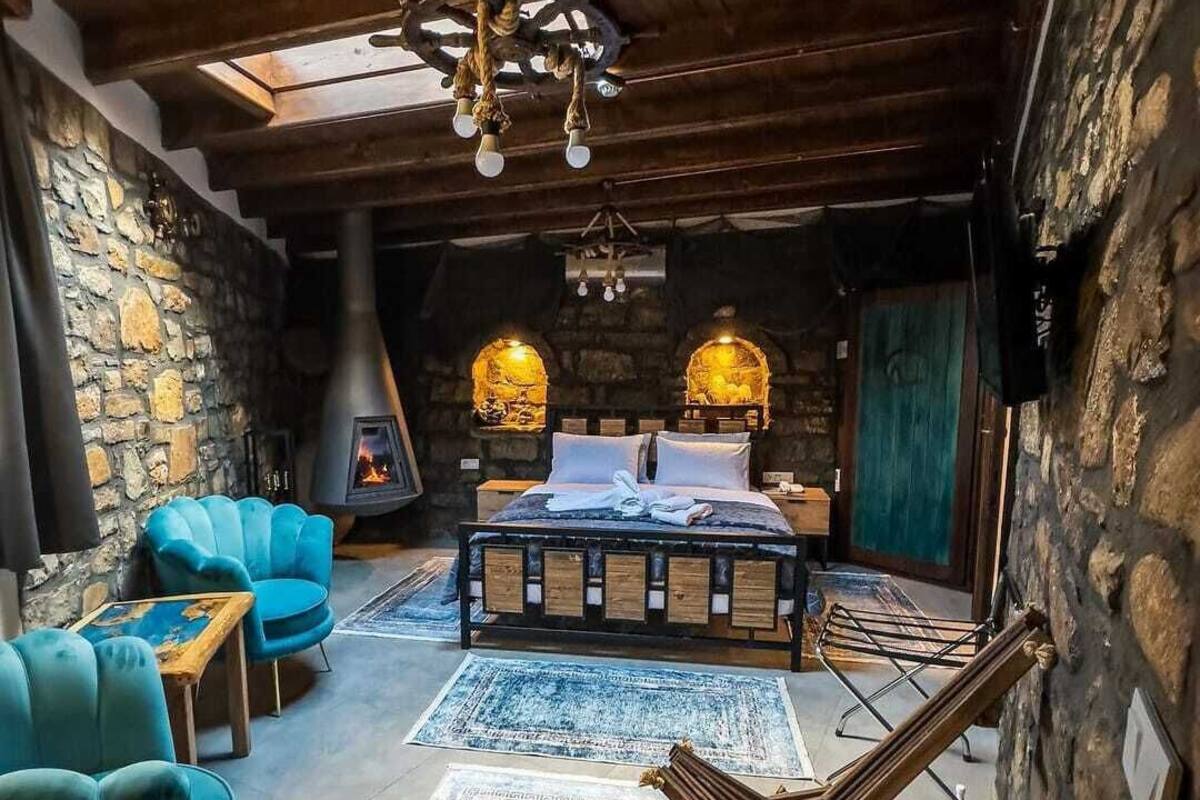 Um quarto acolhedor com parede de pedra, lareira, cama e uma poltrona azul.