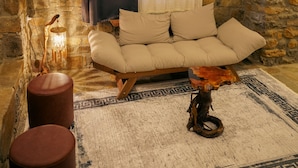 Ein gemütliches Zimmer mit einer Steinwand, einem beigen Sofa, zwei hölzernen Hocker und einem gemusterten Teppich.