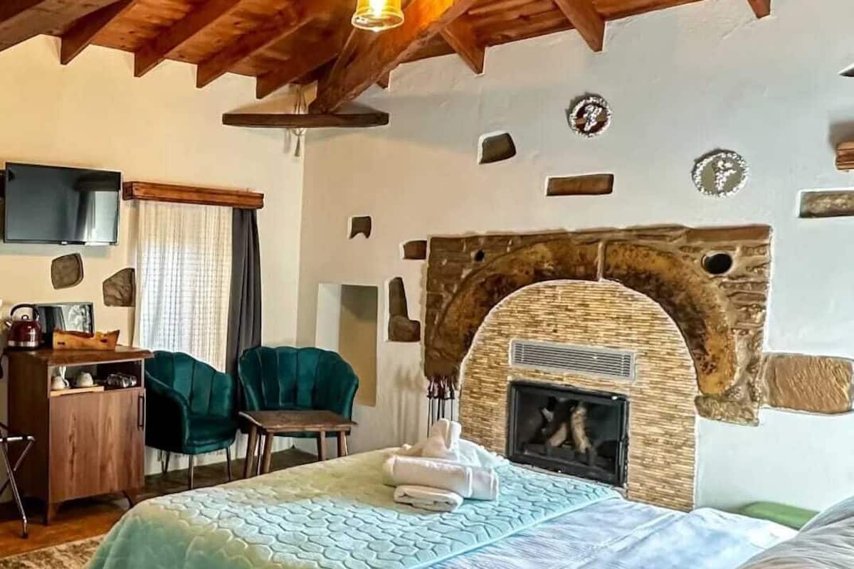 Um quarto acolhedor com uma cama, lareira de pedra, televisão e uma mesa de trabalho com cadeiras.