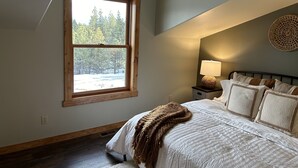 Ein Schlafzimmer mit großem Fenster, einem Bett mit weißer Bettwäsche, einer Nachttischlampe und Wandbehängen aus Gewebe.