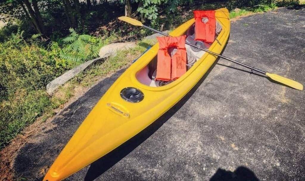 A yellow kayak with two orange life jackets and a paddle on a concrete surface.