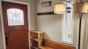 Un banco de madera, una puerta, una lámpara y una ventana en un pasillo.
