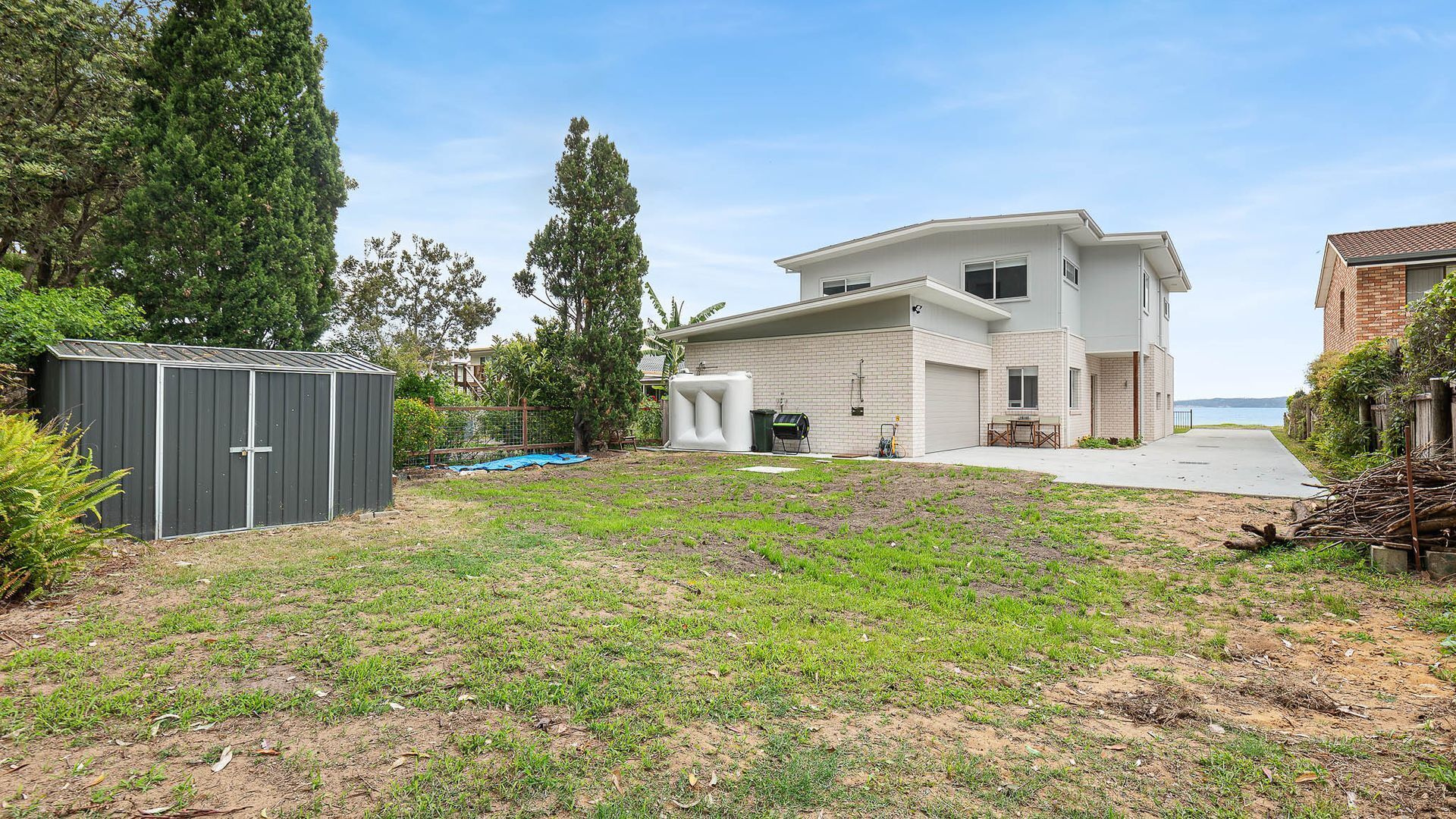 A modern two-story house with a large backyard, a garage, and a view of the sea.