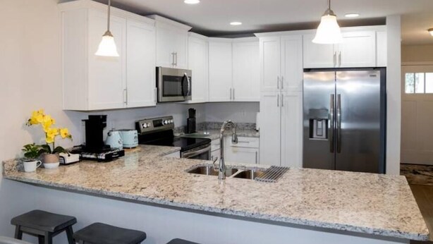 A modern kitchen with white cabinets, stainless steel appliances, granite countertops, and pendant lighting. - Near Airport & Beach Fully Fenced House (Jacksonville)