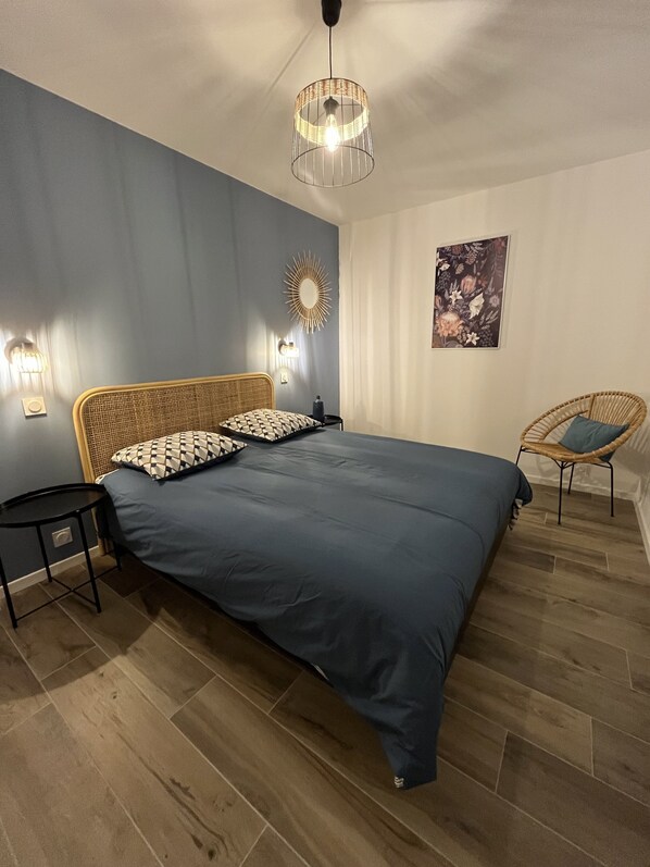 Une chambre à coucher avec un grand lit, une table de chevet, une chaise, une lampe fixée au mur et un miroir décoratif.