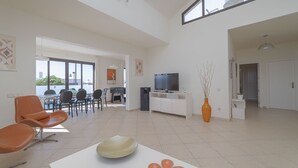Un vaste espace de vie comprenant une table à manger, des chaises orange, un téléviseur à écran plat et une grande fenêtre.