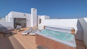 Une terrasse sur le toit équipée d’un jacuzzi, de chaises longues et d’une entrée avec une porte en verre.