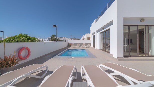 Un espace piscine aménagé sur le toit, avec des chaises longues, une piscine et un bâtiment doté de grandes fenêtres.