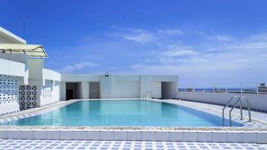 A rooftop swimming pool with clear blue water, surrounded by a tiled deck and a white building with a covered entrance. - Angani Apartment : 3 Bedroom all-ensuite apartment in Mombasa (Mombasa)