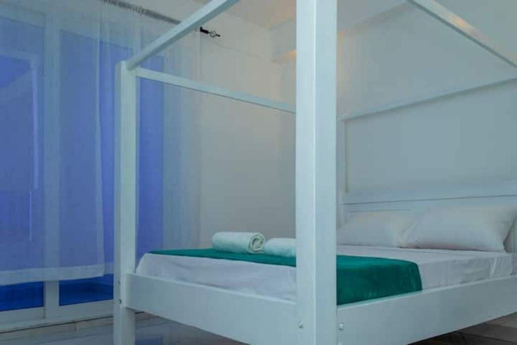 Ein weißes Bett mit Baldachin, ein grünes Handtuch und ein weißes Kopfkissen in einem Zimmer mit blau-weißer Farbgebung.