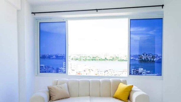 A room with a white sofa, a yellow pillow, and a large window with a city view. - Angani Apartment : 3 Bedroom all-ensuite apartment in Mombasa (Mombasa)