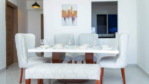 A dining area with a white table set for four, surrounded by upholstered chairs with wooden legs. - Angani Apartment : 3 Bedroom all-ensuite apartment in Mombasa (Mombasa)