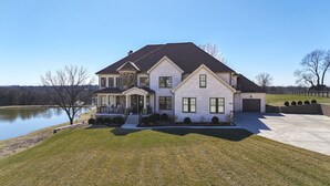 Une maison à deux étages avec une grande véranda à l’avant, un garage et une vue sur le lac.