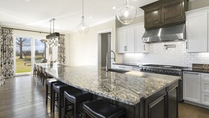 Une cuisine moderne dotée d’un grand îlot central, d’appareils électroménagers en acier inoxydable et de luminaires suspendus.