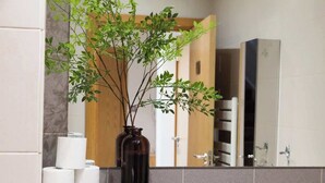 A bathroom with a mirror, a vase with green plants, and toilet paper on the counter.