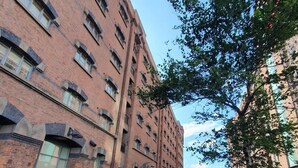 A multi-story brick building with a central courtyard, surrounded by greenery and a pedestrian pathway.