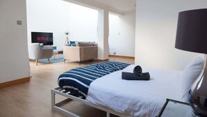 A modern hotel room with a bed, a desk, a chair, a TV displaying 'NETFLIX', and a lamp.