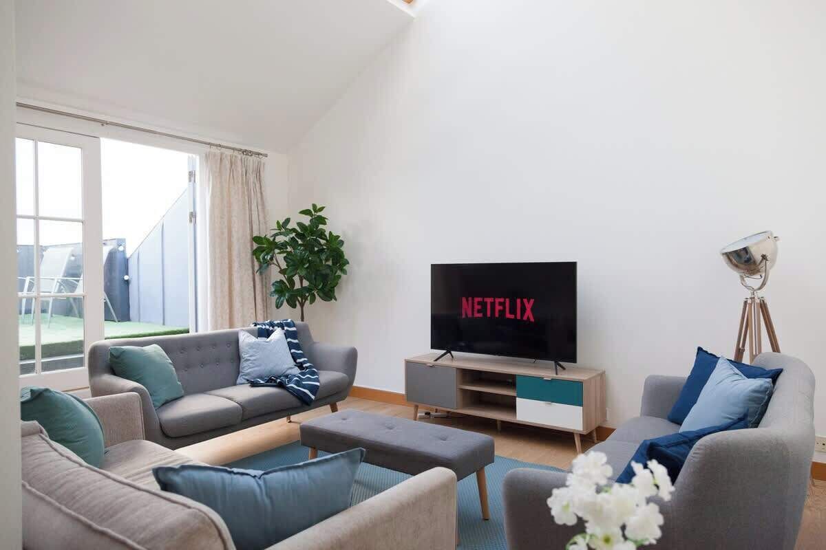 Un soggiorno con una TV a schermo piatto che mostra 'NETFLIX', un divano grigio, un tavolino da caffè e una pianta in vaso.
