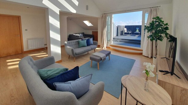 A spacious living area with a high ceiling, a sofa set, a coffee table, and a view of the outdoors through large windows.