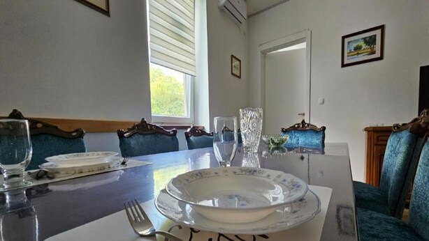 A dining area with a table set for four, blue upholstered chairs, and a window with blinds.