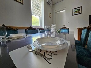 A dining area with a table set for four, blue upholstered chairs, and a window with blinds. - Apartment Gracac - Two Bedroom Apartment with Terrace (Gracac)