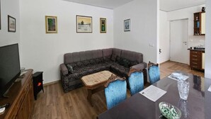 A living room with a sofa, a coffee table, a TV, and a dining area with a table and chairs.