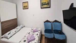 A bedroom with a bed, two chairs, a TV, and two framed pictures on the wall.