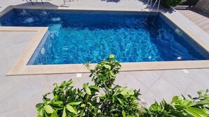 A rectangular swimming pool with clear blue water, surrounded by a tiled deck and a small green shrub in the foreground. - Luxury apartment Ani - Three Bedroom Apartment with terrace and Swimming pool (Sutivan)