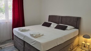 A neatly made bed with pillows, a bedside lamp, and a window with red curtains. - Luxury apartment Ani - Three Bedroom Apartment with terrace and Swimming pool (Sutivan)