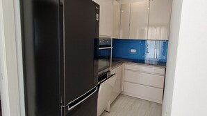 Una cocina pequeña con un refrigerador negro, armarios blancos y un salpicadero azul.