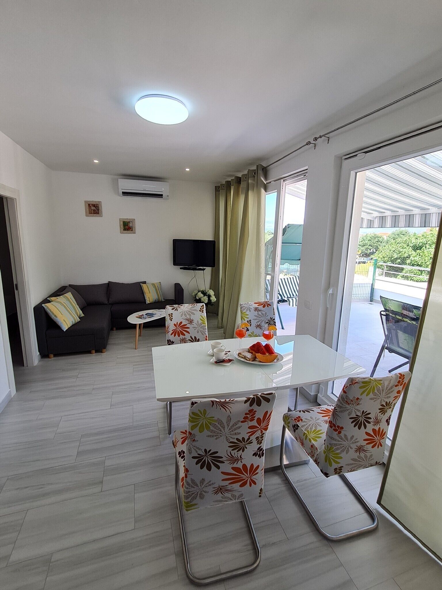 Un salon moderne comprenant un canapé, un téléviseur à écran plat, une table à manger avec des chaises et un balcon avec vue.